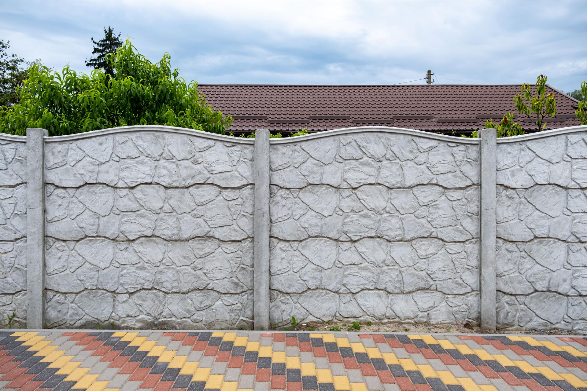 Decorative concrete fence on the background of green trees.