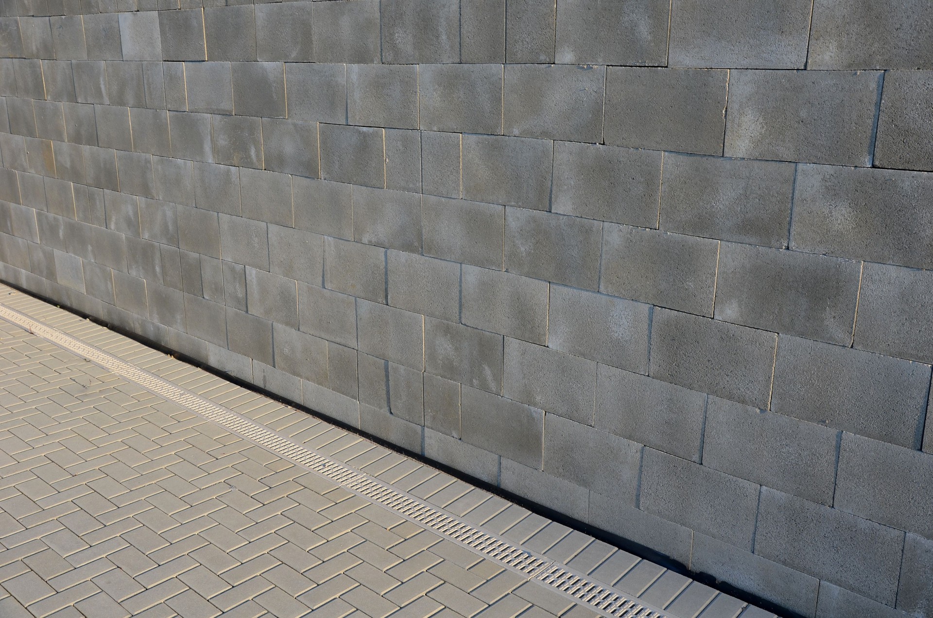 concrete wall made of smooth blocks. high dividing noise wall of the yard. under the wall is a longitudinal channel with a grid for drainage interlocking paving